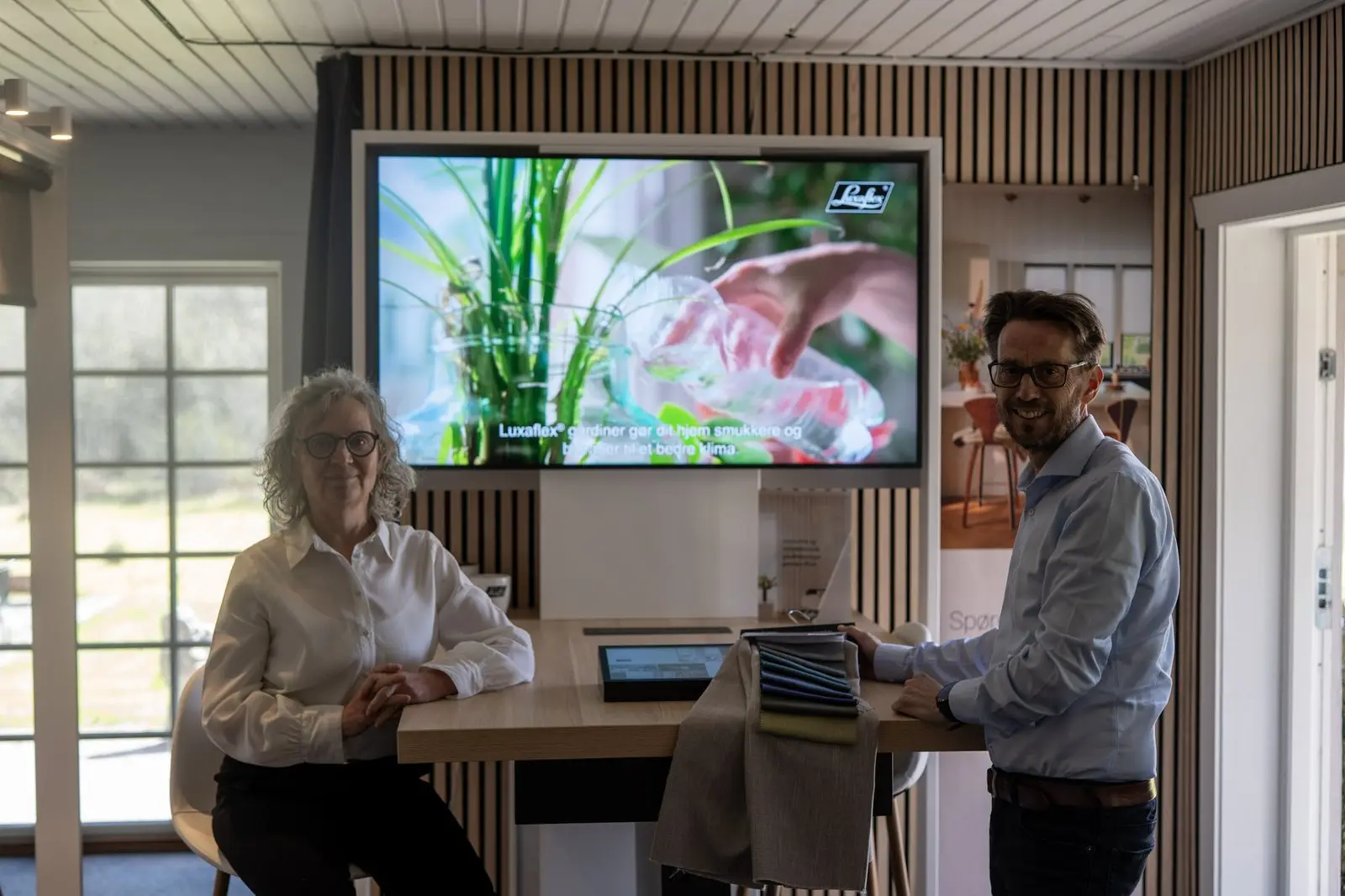 Jan og Lotte med stofprøver i showroomet foran Luxaflex-skærmen