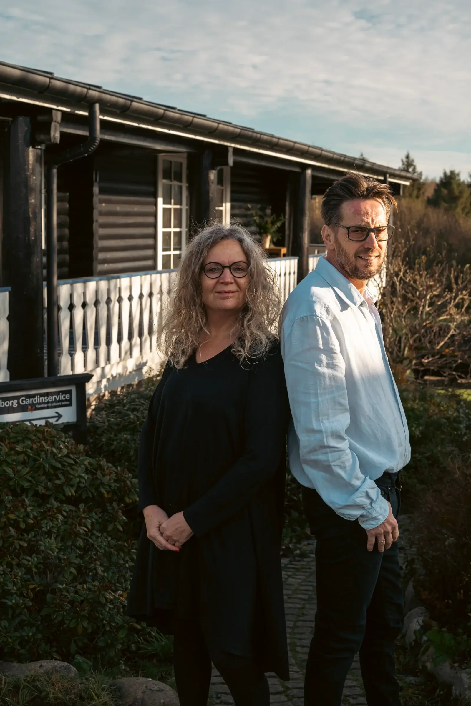 To personer foran en træbygning i solskin.