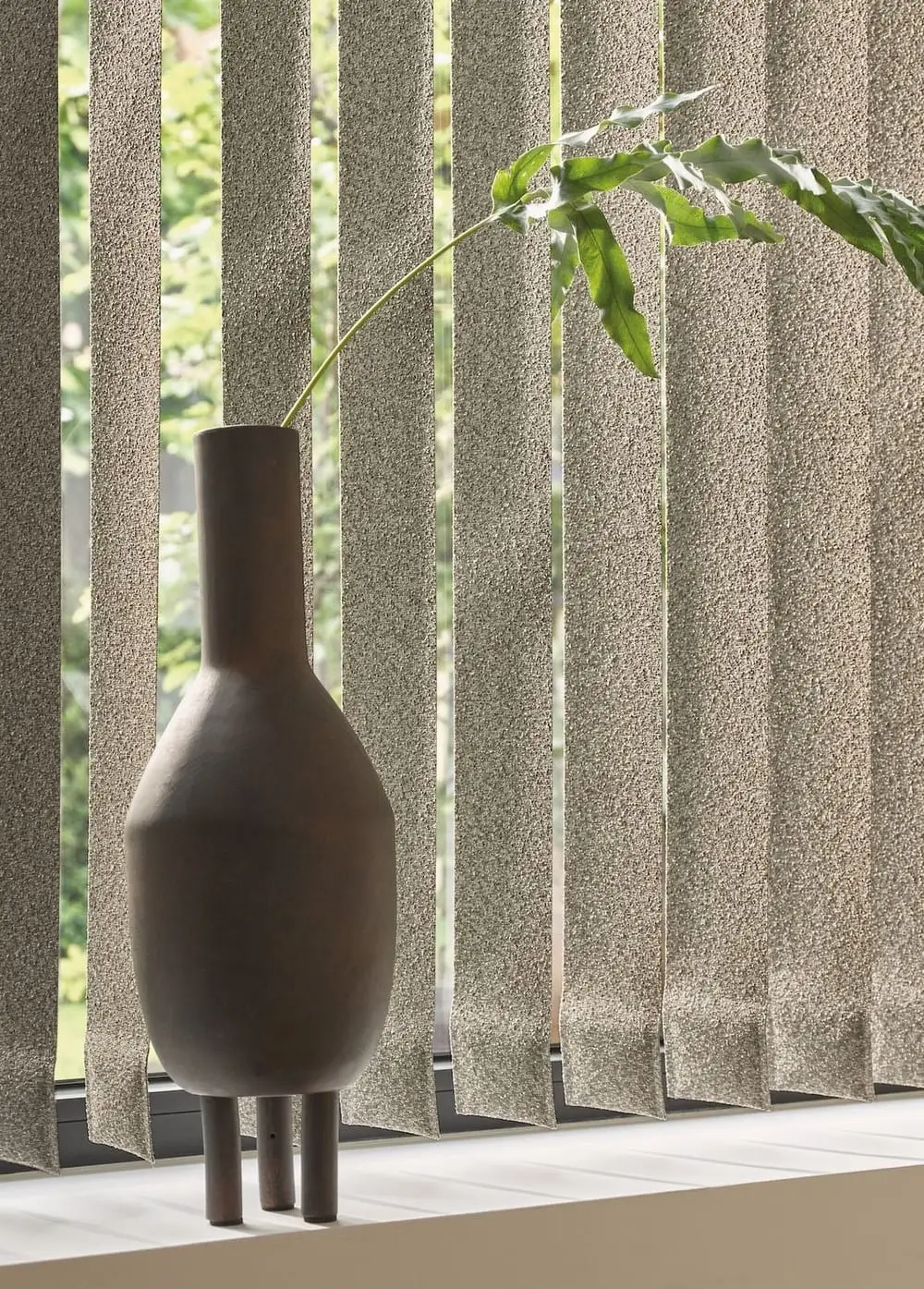 Vase med grøn plante foran lyse gardiner