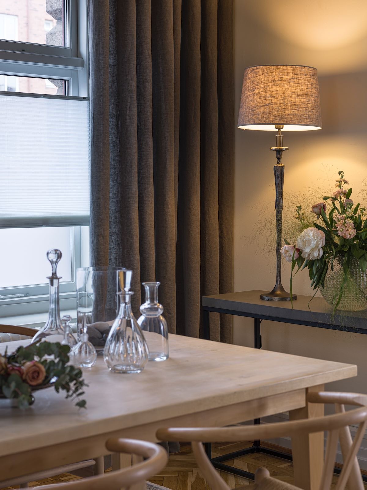 Spisestue med lampe, karafler og blomsterarrangement.